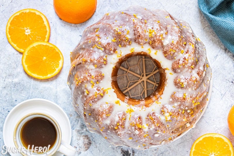 Overhead shot of orange bundt cake with orange glaze, with coffee cup at the side.