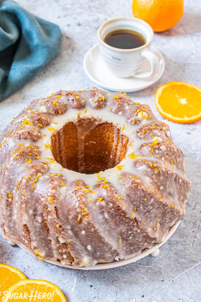 Orange bundt cake with orange glaze, with coffee cup and teal napkin in background.