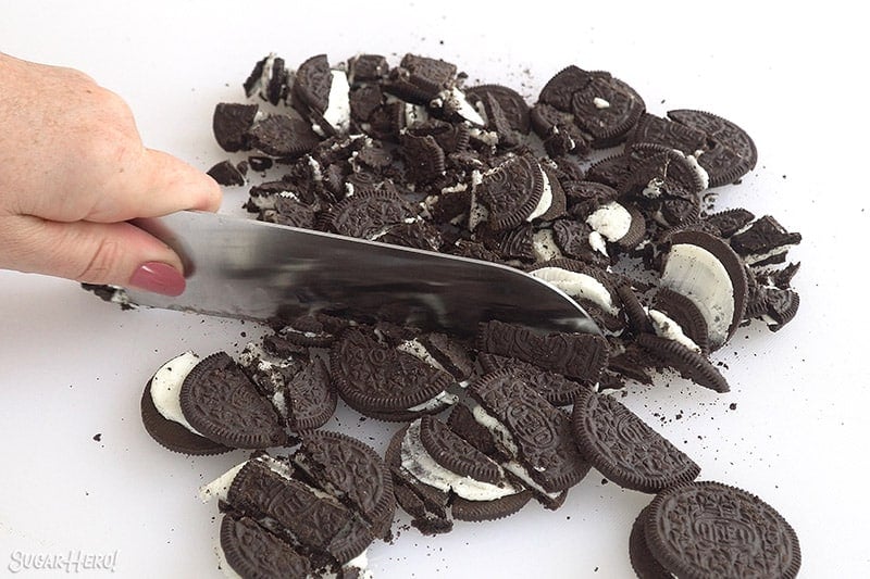 Large knife slicing Oreos on a white cutting board.