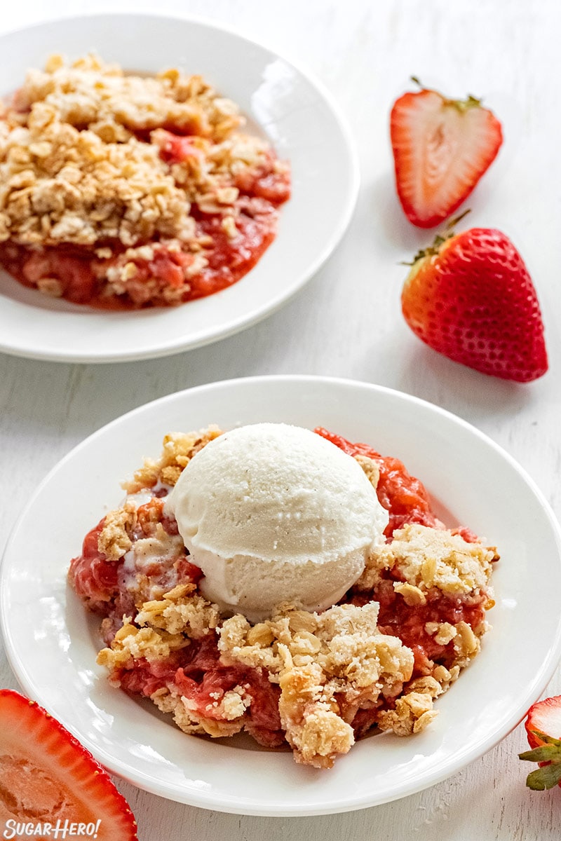 Two servings of Strawberry Crisp in white bowls with vanilla ice cream.