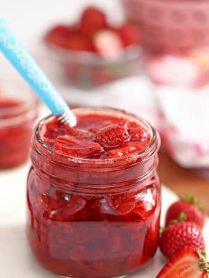 Glass jar of Strawberry Sauce with a blue spoon sticking out.