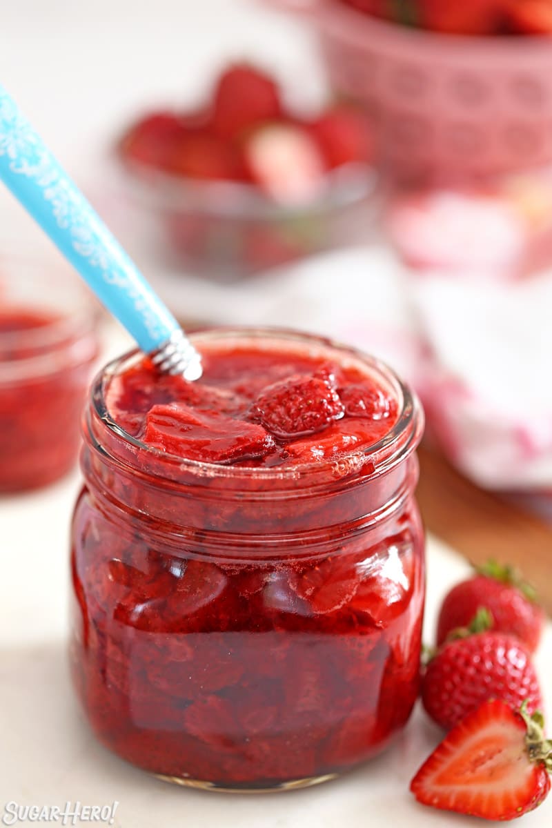 Glass jar of Strawberry Sauce with a blue spoon sticking out.