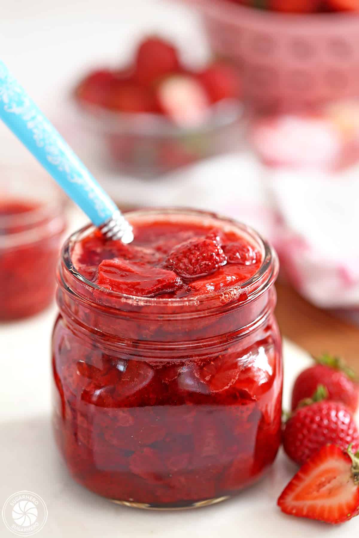 Glass jar of Strawberry Sauce with a blue spoon sticking out.