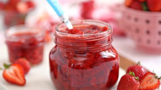 Glass jar of Strawberry Sauce with a fresh strawberries scattered around.