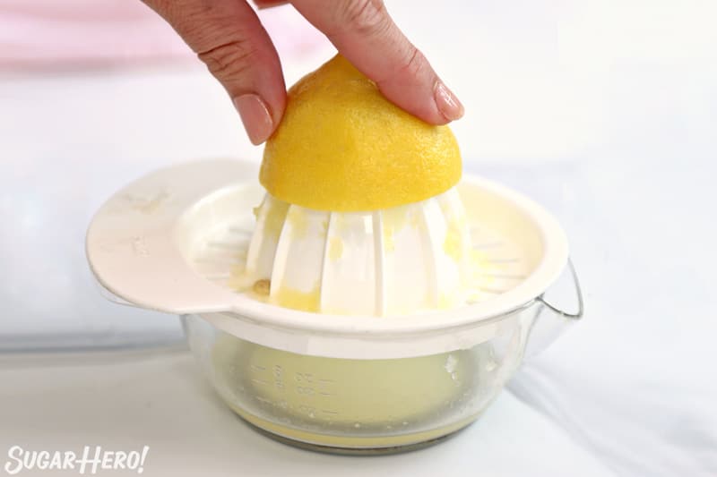 Juicing half of a lemon using a white hand juicer.