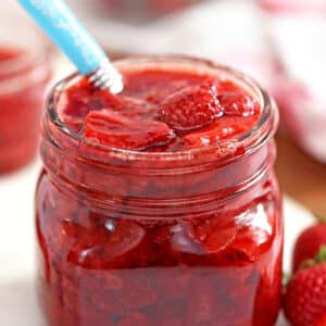 Glass jar of Strawberry Sauce with blue spoon sticking out.