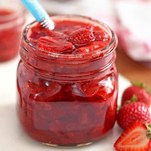 Glass jar of Strawberry Sauce with blue spoon sticking out.