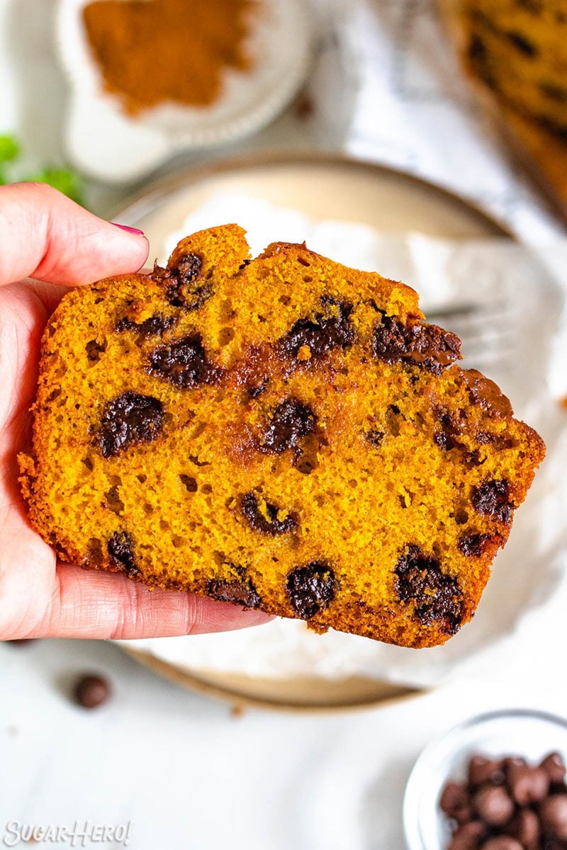 Hand holding a slice of pumpkin bread studded with melted chocolate chips.