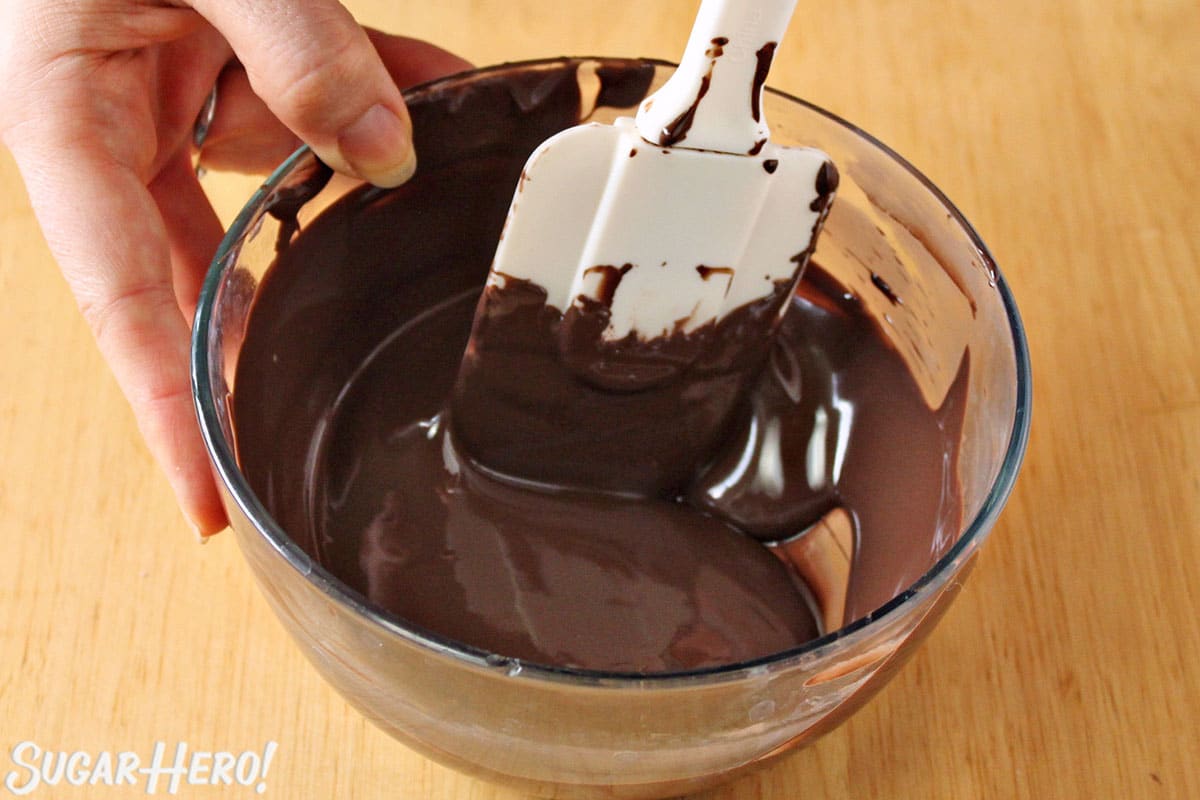 Stirring melted chocolate in a glass bowl.