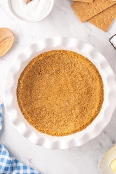 Photo of graham cracker crust in white pie dish with ingredients around the pie dish.