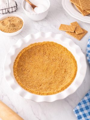 Graham Cracker Crust in a fluted white pie pan with ingredients surrounding it.