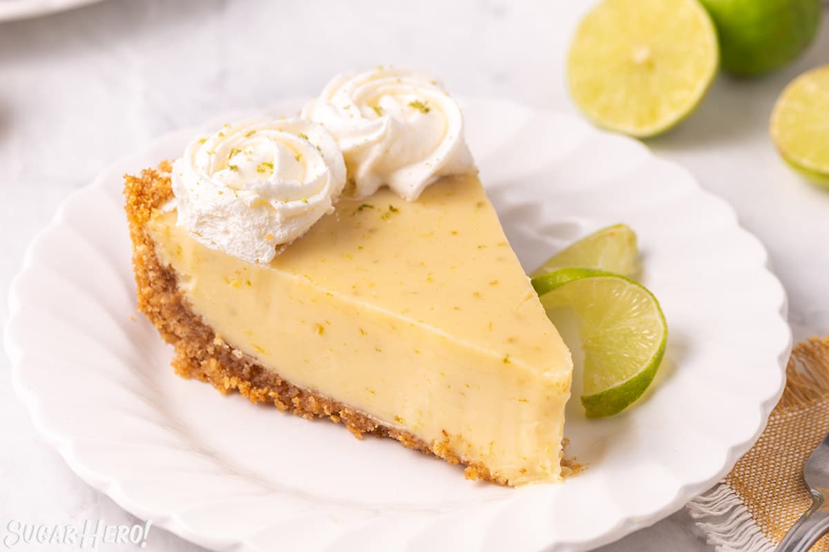 Key Lime Pie slice on a white plate with a twist of lime next to it.