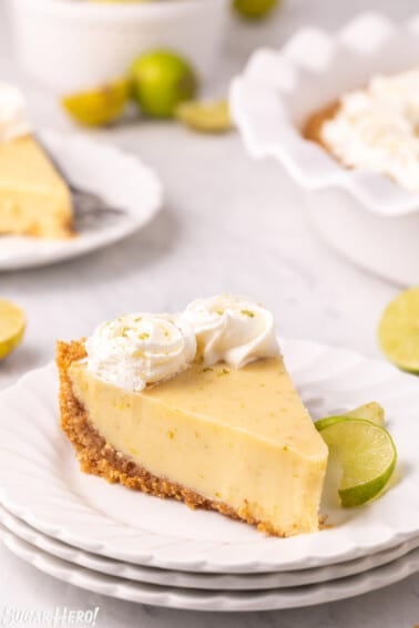 Slice of Key Lime Pie on stack of white plates with more pie slices in the background.