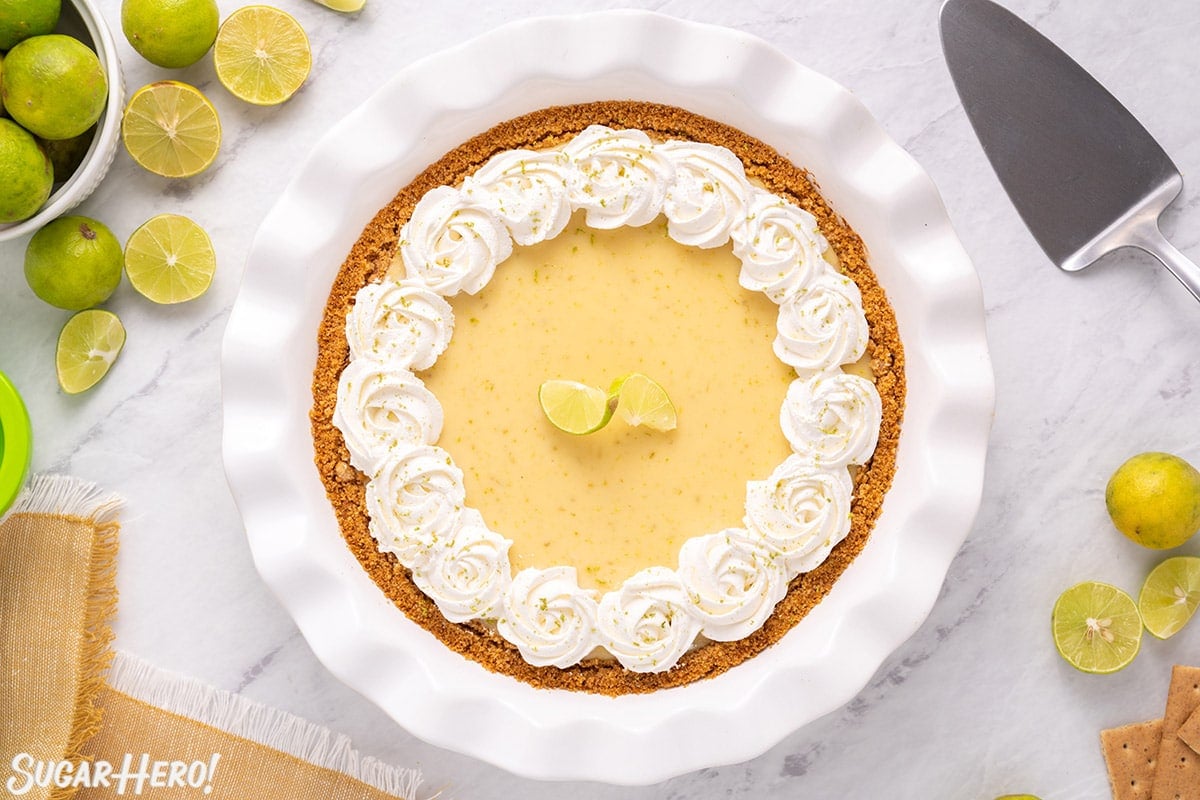 Overhead shot of Key Lime Pie in white pie pan, decorated with whipped cream and a twist of lime.
