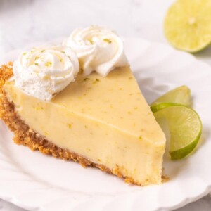 Slice of Key Lime Pie on white plate with a twist of lime on the side.