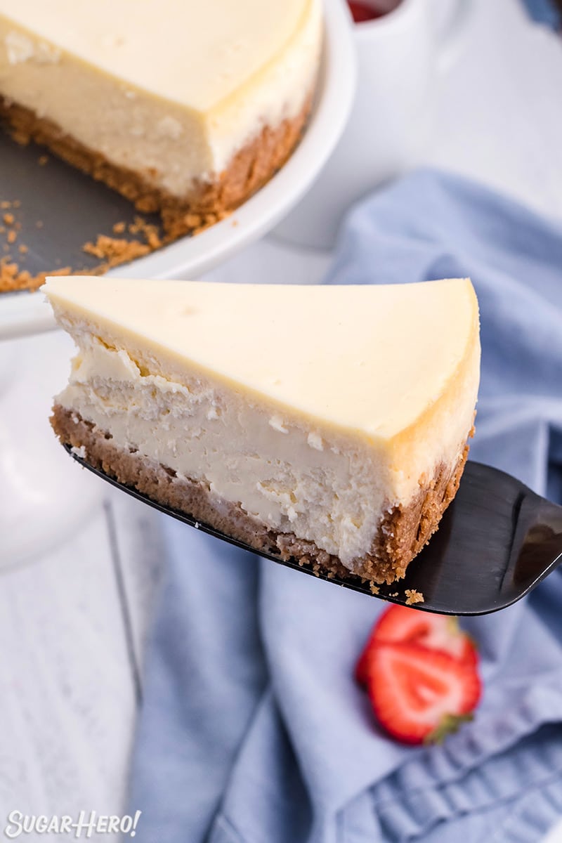 Cake server removing a single slice of New York Style Cheesecake.