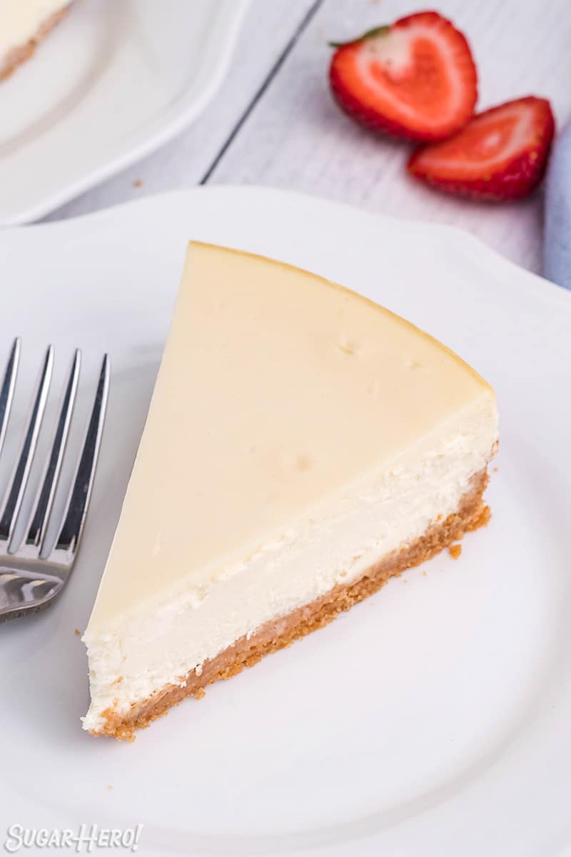 Slice of plain New York Style Cheesecake on a white plate with a fork next to it.