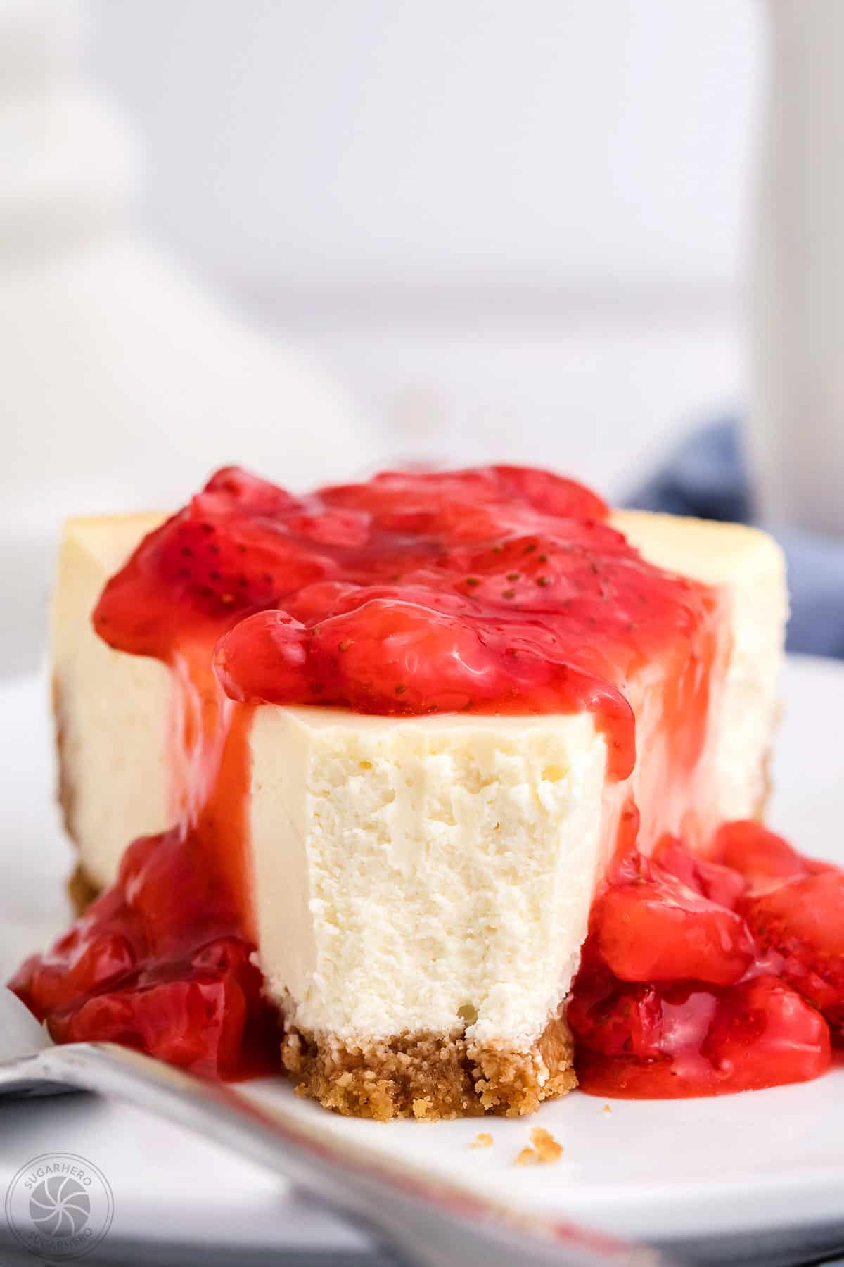 Close-up slice of white cheesecake with strawberry sauce on top and a bite taken out of it.