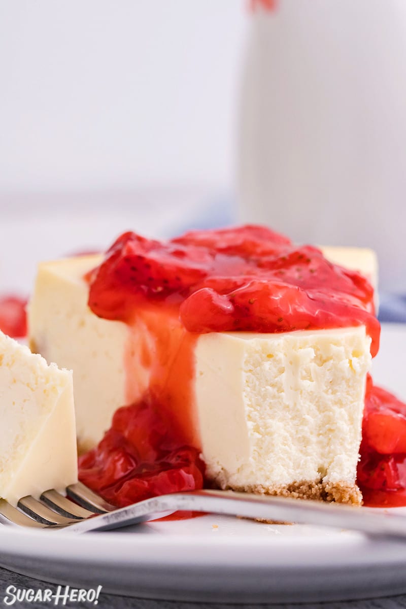 Slice of white cheesecake with strawberry sauce on top and a bite taken out of it.