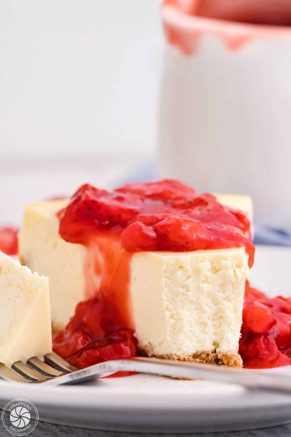 Slice of white cheesecake with strawberry sauce on top and a bite taken out of it.