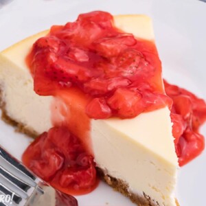 Slice of cheesecake on a white plate with strawberry sauce dripping down the sides.