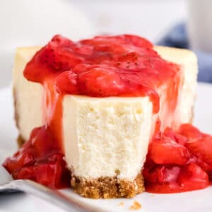 Slice of New York Style Cheesecake on a white plate with strawberry sauce on top.