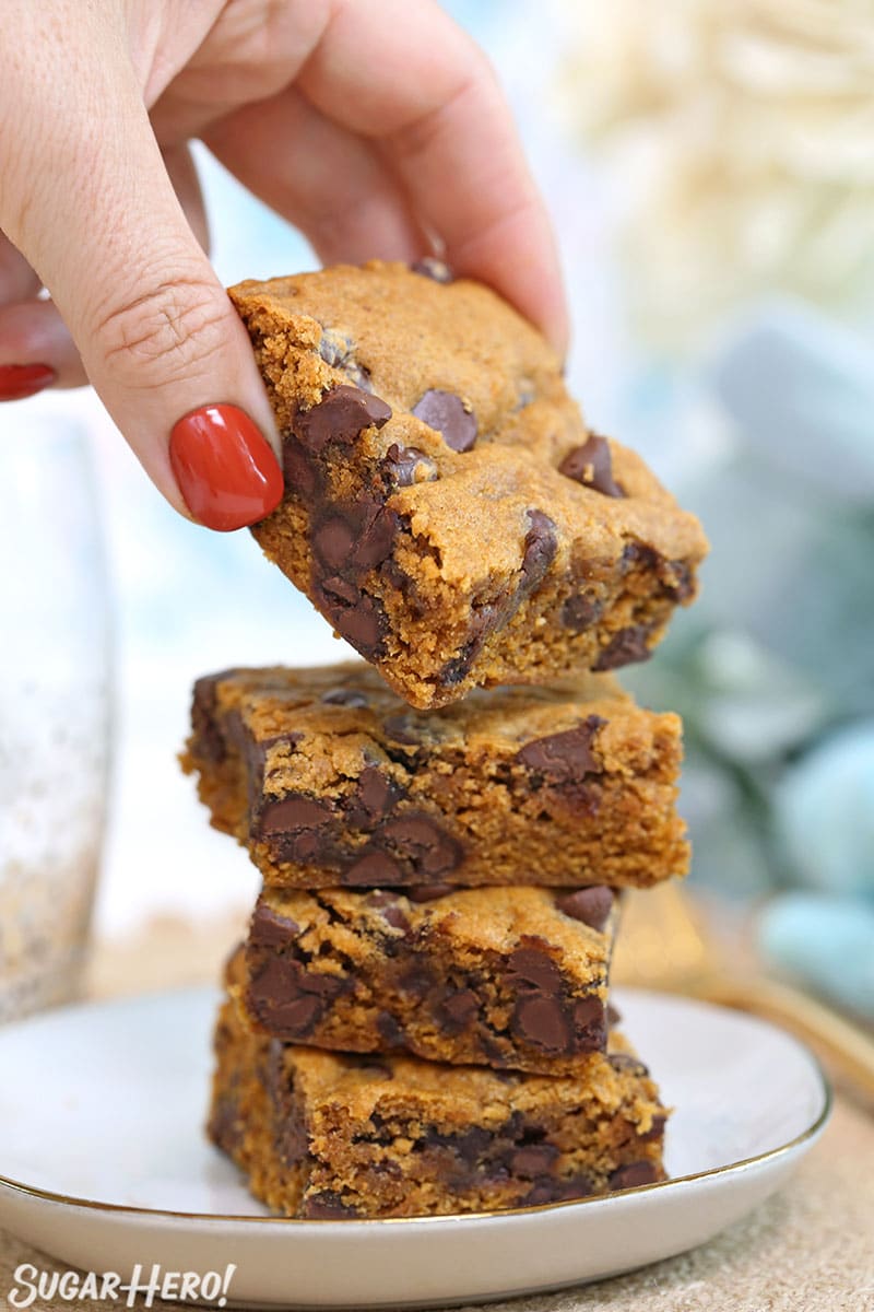 Hand reaching in a grabbing a Pumpkin Chocolate Chip Bars from on top of a stack of bar cookies.