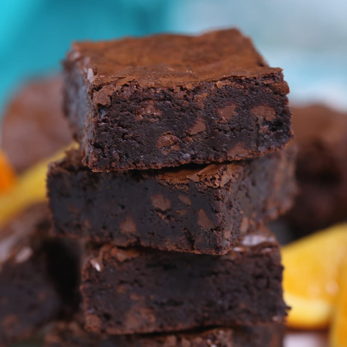 Stack of four chocolate orange brownies with orange slices alongside them.