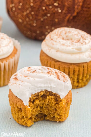 Three pumpkin spice cupcakes, the one in the front has a bite taken out of it.