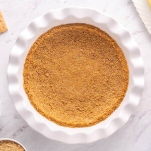 Graham cracker crust in a white pie pan with scalloped edges.