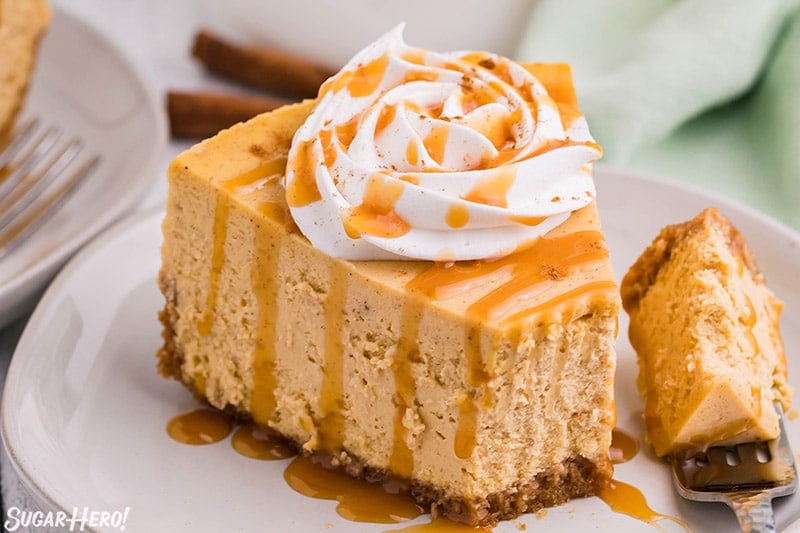 Slice of pumpkin spice cheesecake topped with whipped cream and caramel sauce.