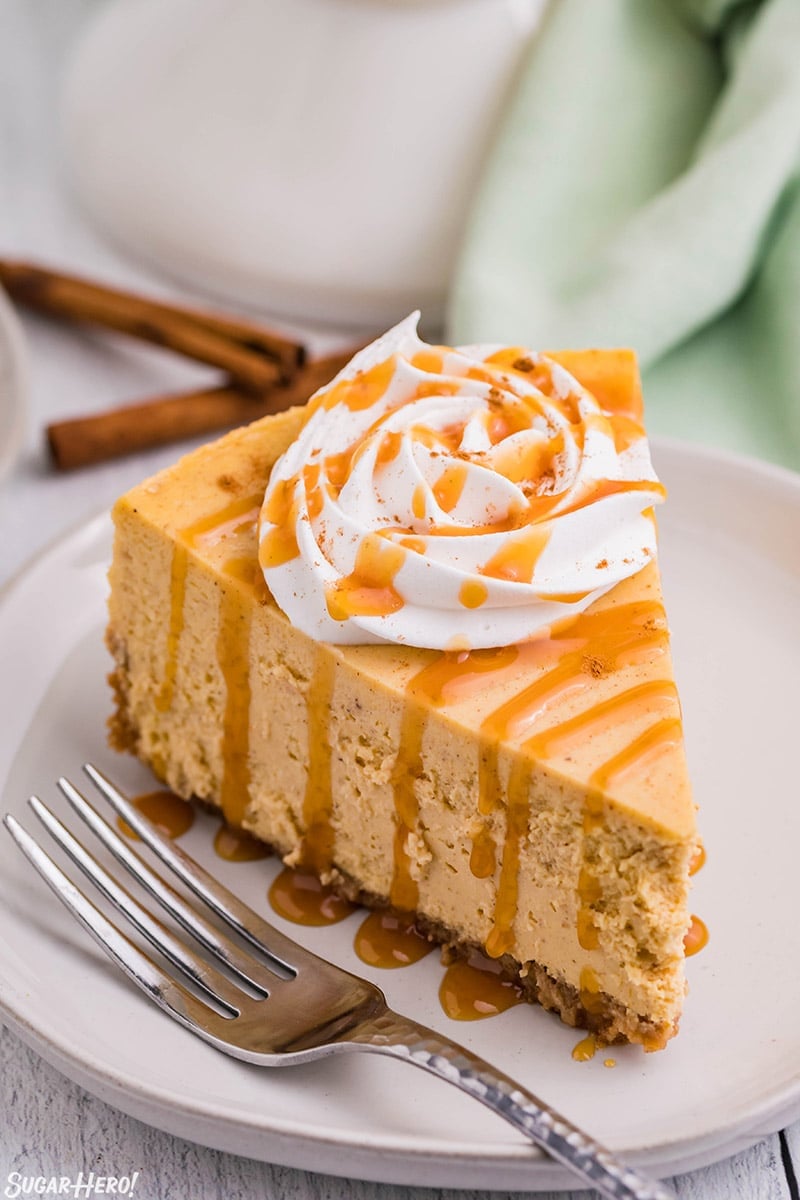 Slice of pumpkin spice cheesecake topped with whipped cream and cinnamon on a plate with a fork beside it.