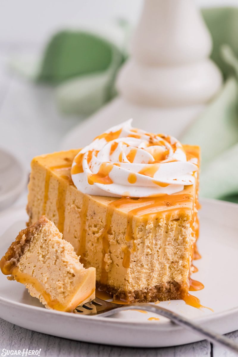 Slice of pumpkin spice cheesecake with a bite taken and set next to it on a fork on a round white plate.