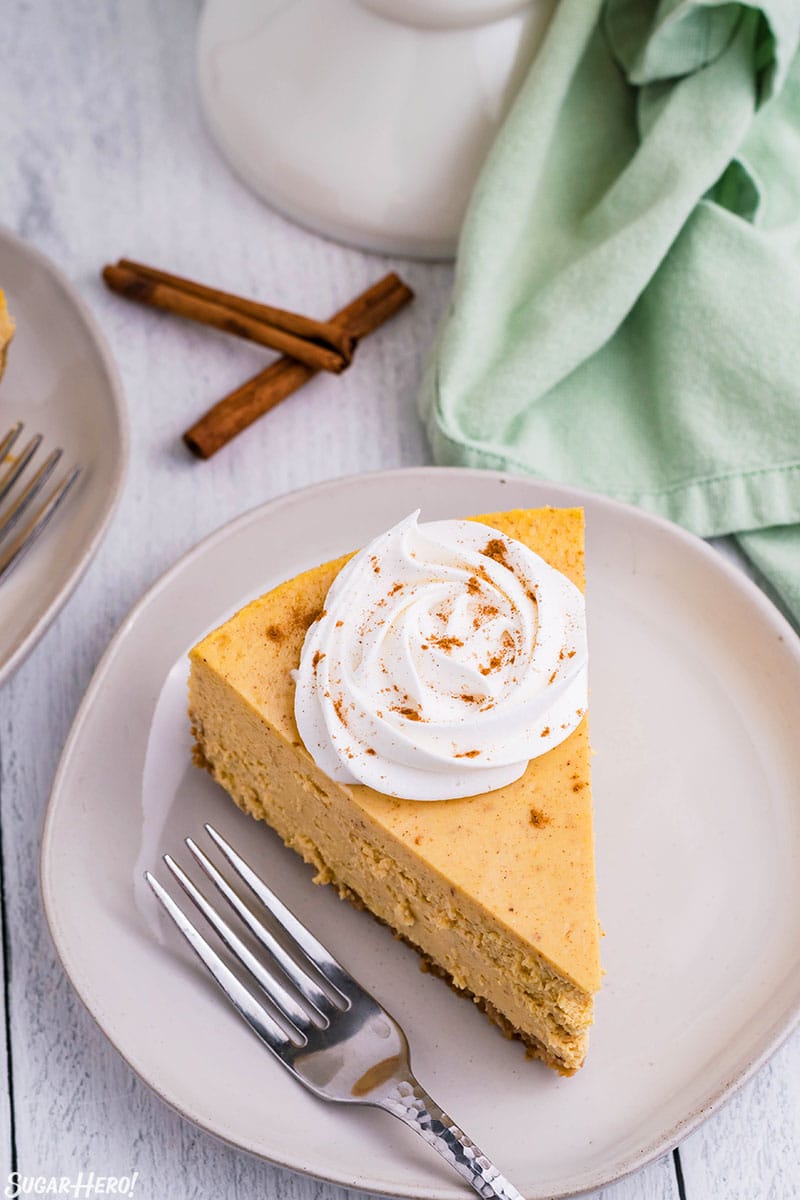 Slice of pumpkin spice cheesecake topped with a rosette of whipped cream and cinnamon.