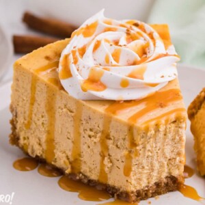 Slice of pumpkin spice cheesecake topped with a rosette of whipped cream and caramel sauce.