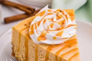 Slice of pumpkin spice cheesecake topped with whipped cream and caramel sauce.