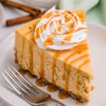 Slice of pumpkin spice cheesecake topped with whipped cream and caramel sauce with a fork next to it.