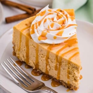 Slice of pumpkin spice cheesecake topped with whipped cream and caramel sauce with a fork next to it.