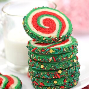 Stack of red, white, and green Christmas pinwheel cookies and a mug of milk.