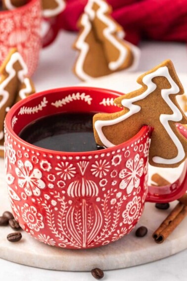 Tree-shaped gingerbread cookie on the lip of a red mug.