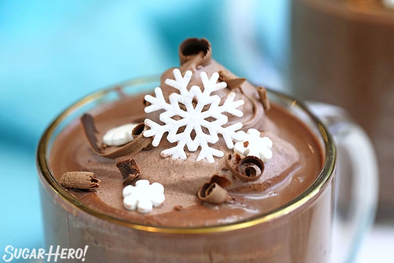 Close-up of Peppermint Hot Chocolate mug topped with cocoa whipped cream, chocolate shavings, and edible snow flakes.