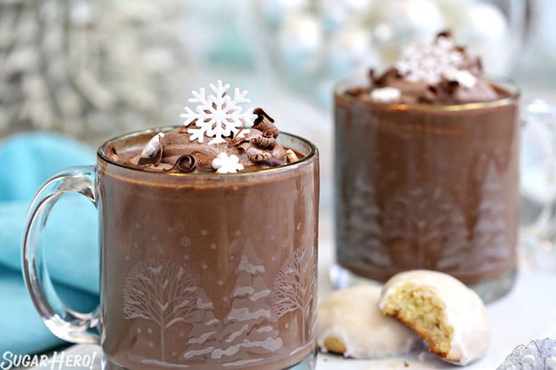 Two mugs of Peppermint Hot Chocolate topped with cocoa whipped cream and edible snowflakes.