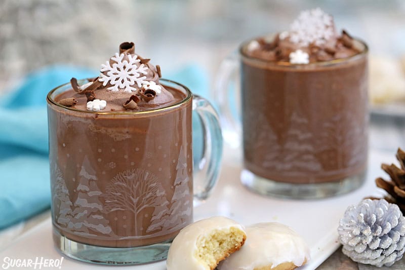 Two mugs of Peppermint Hot Chocolate topped with cocoa whipped cream and edible snowflakes.