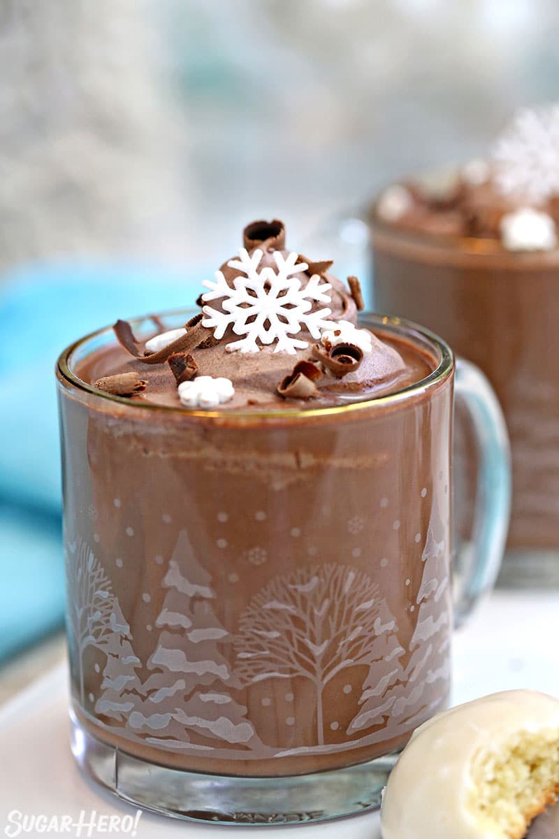 Peppermint Hot Chocolate in a clear glass mug topped with cocoa whipped cream and edible snowflakes.