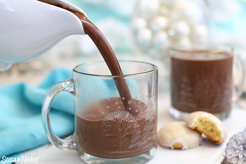 Pouring peppermint hot chocolate into a glass mug with a gold rim.