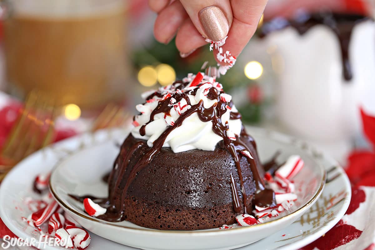 Hand sprinkling chopped candy canes on top of Peppermint Lava Cakes topped with whipped cream.