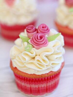 Pink cupcake with white ruffled frosting and pink fondant flowers.