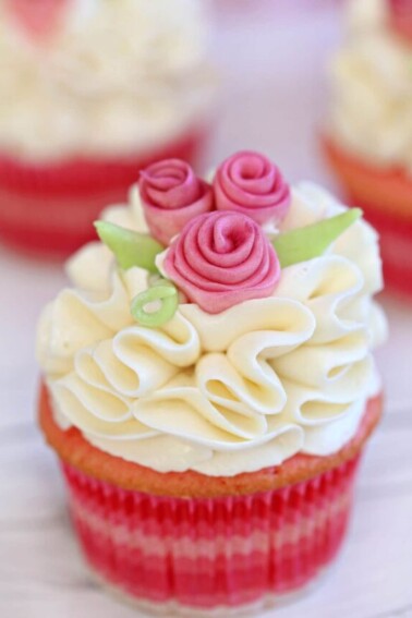 Pink cupcake with white ruffled frosting and pink fondant flowers.