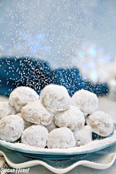 Plate of Pecan Snowball Cookies with powdered sugar being sprinkled on it.