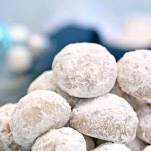 Plate of Pecan Snowball Cookies with powdered sugar being sprinkled on it.